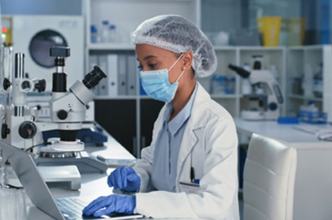 Scientist in a laboratory working on a laptop, surrounded by microscopes and lab equipment, conducting research related to cell and gene therapy.